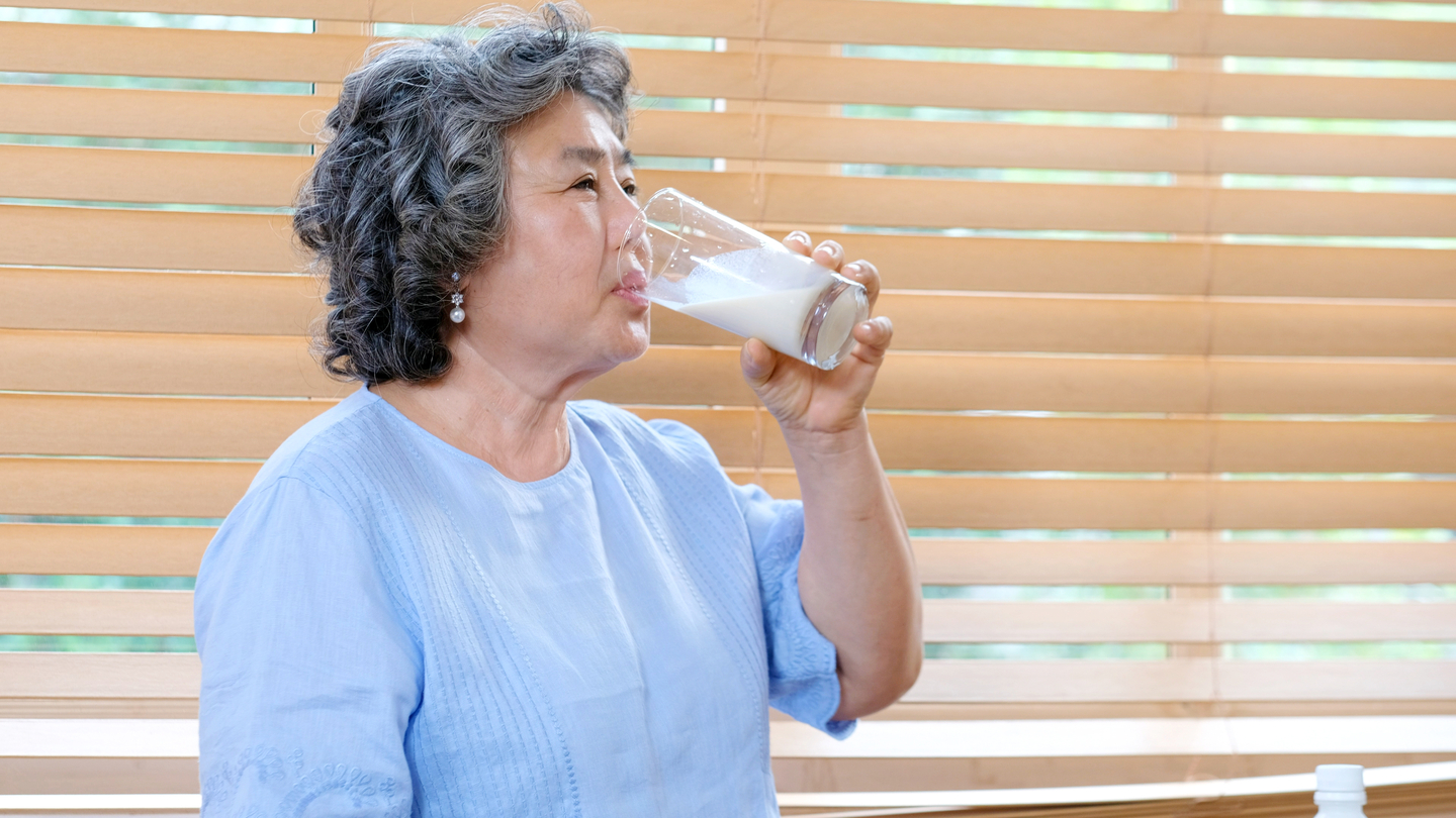Senior,asian,woman,drinking,milk,at,kitchen,home,in,the